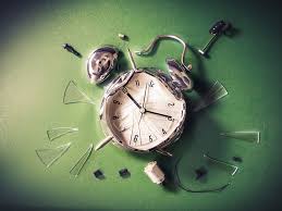 Broken alarm clock with scattered pieces on a green surface.