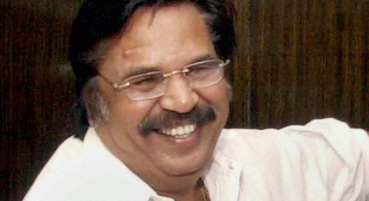 Smiling man with glasses and a mustache wearing a white shirt, looking slightly to the left.