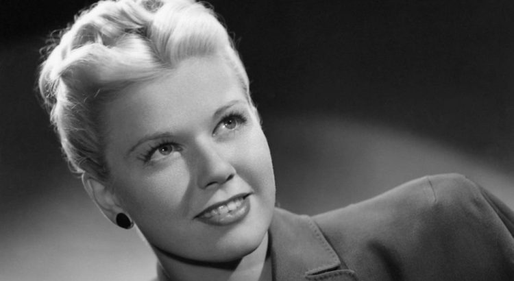 Black-and-white portrait of a smiling woman with short blonde hair, looking upward to the left.