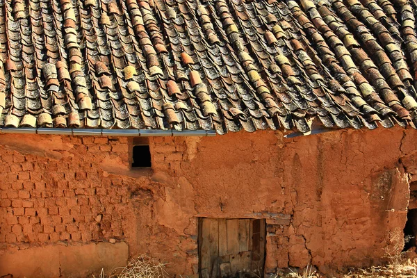 Old adobe house with red, sun-baked walls, a weathered wooden door, and a tiled roof.