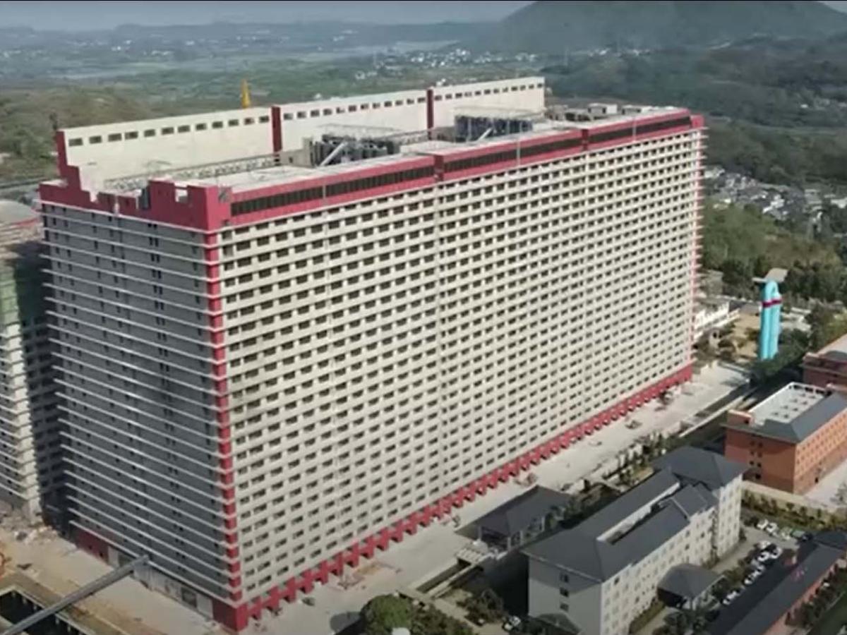 Aerial view of a large beige hotel with red trim, tall and rectangular, with a blue statue nearby and surrounding buildings.